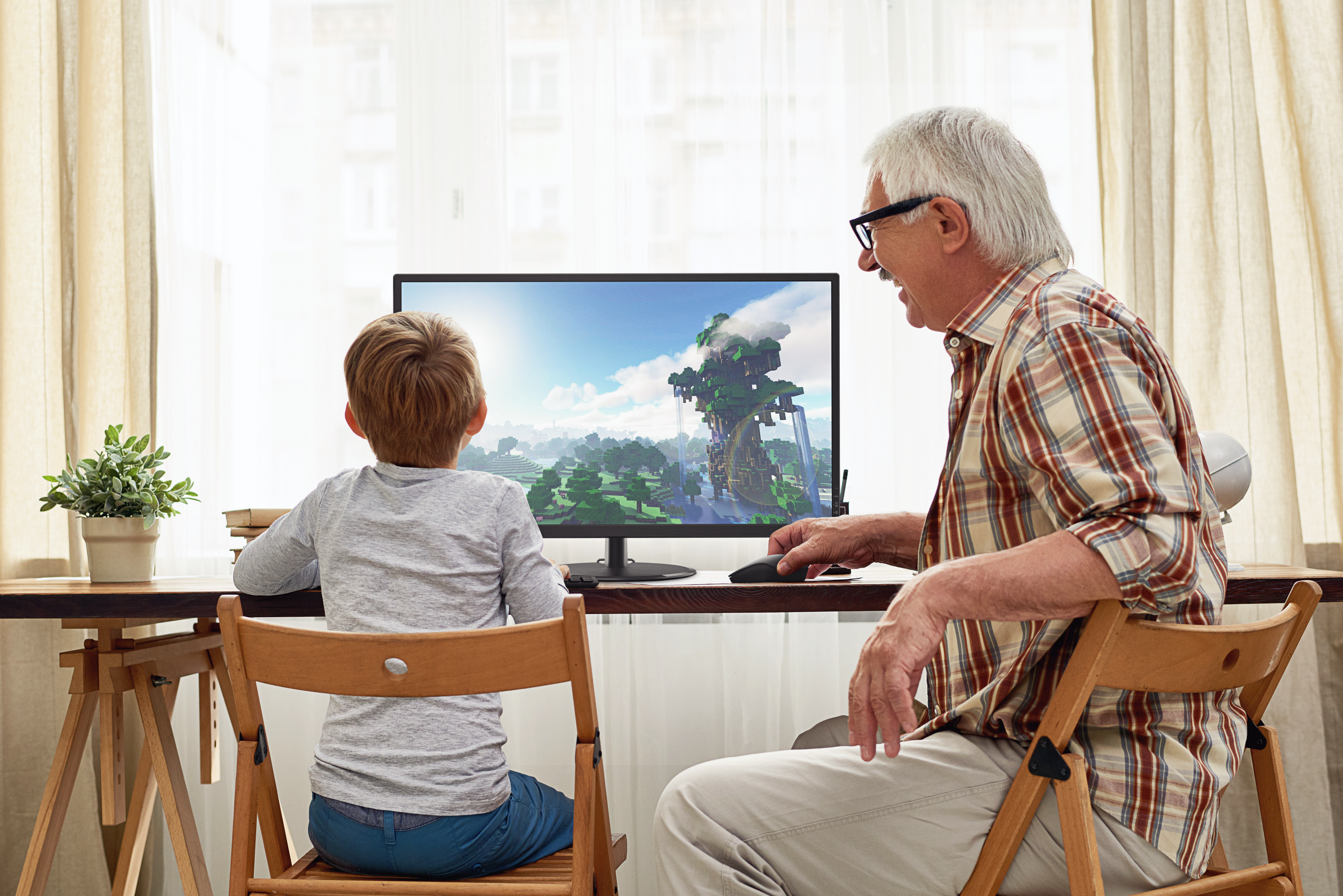 Älterer Mann und Junge spielen zusammen Videospiele am Computer in einem hellen Zimmer.