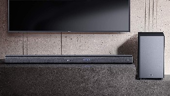 Barra de sonido y subwoofer en una superficie de piedra, con un televisor al fondo.