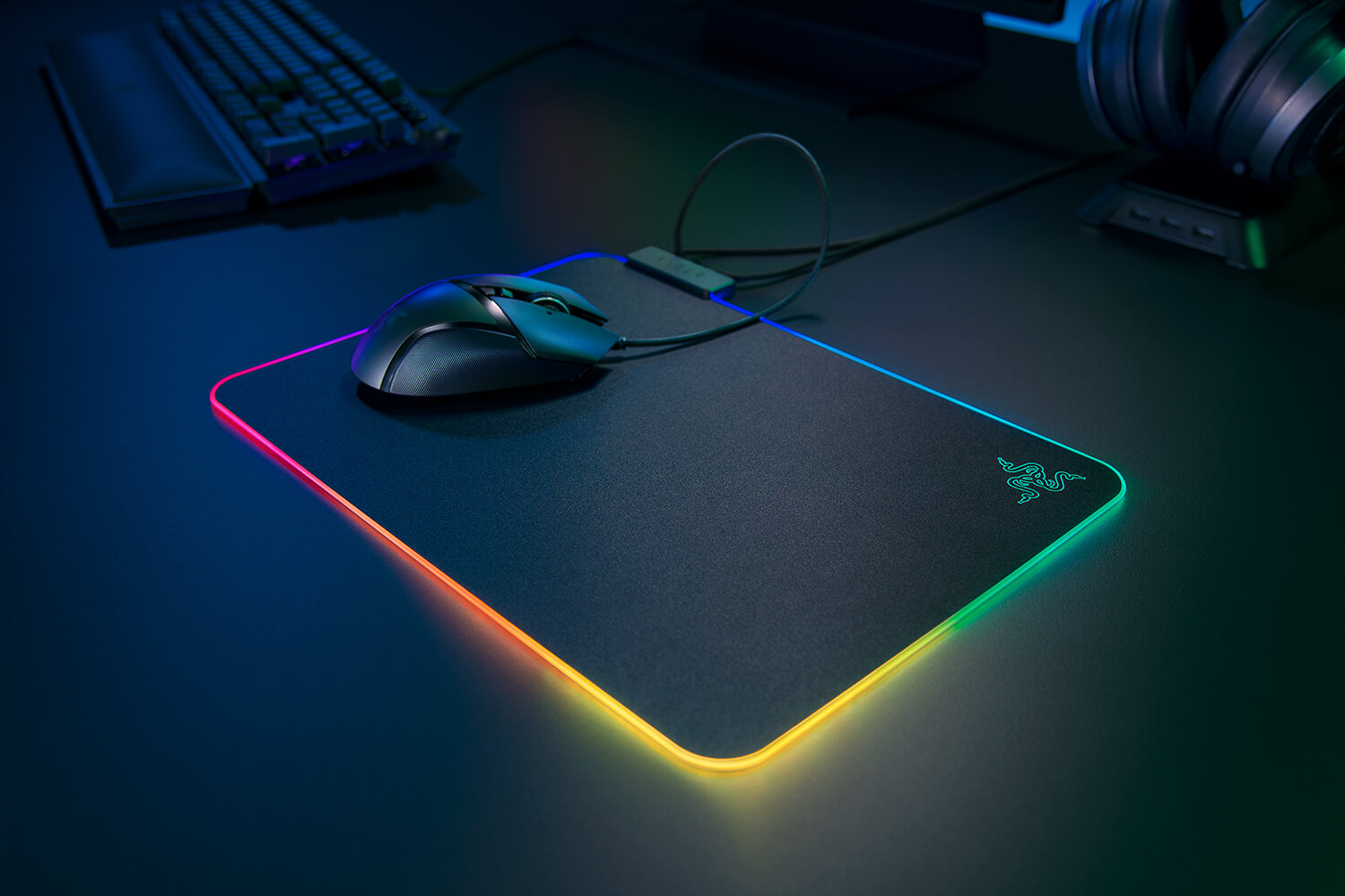 Souris de jeu noire sur un tapis de souris noir avec des lumières de bord colorées. Un clavier et un casque en arrière-plan.