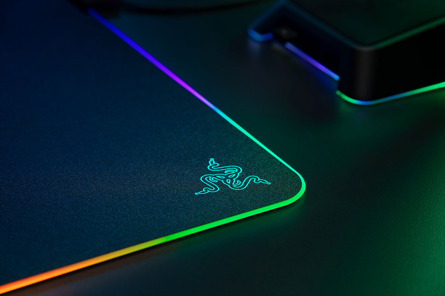 Tapis de souris Razer noir avec bord éclairé montrant des couleurs arc-en-ciel, logo Razer visible.