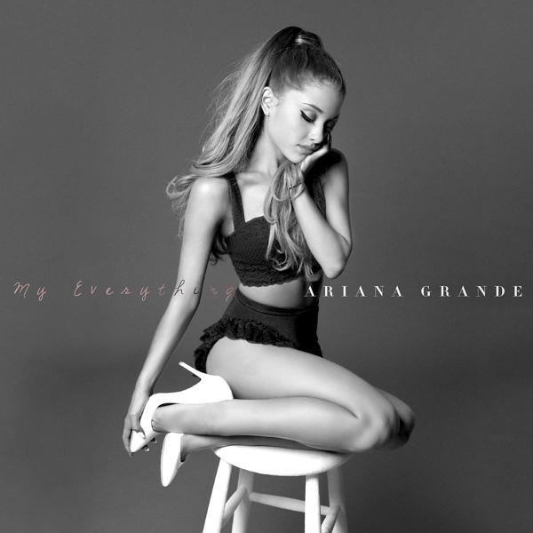 Zwart-wit foto van Ariana Grande in een tweedelige outfit, zittend op een kruk.