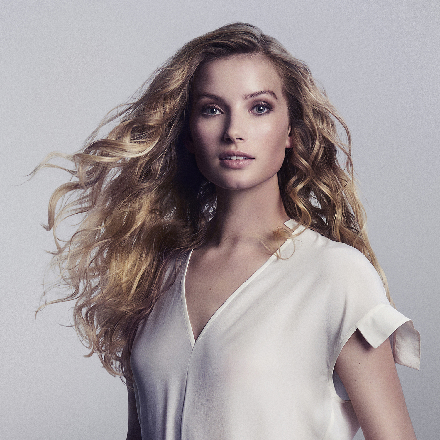 Blonde vrouw met lang golvend haar die naar de kijker kijkt.