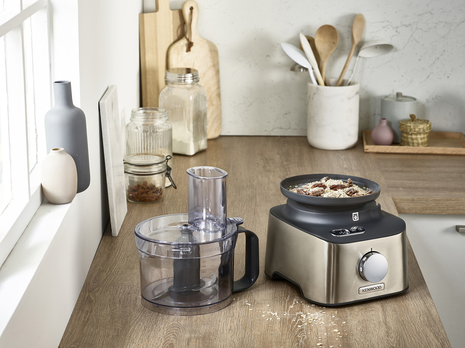 A food processor with a clear container and a stainless steel base, placed on a wooden counter.
