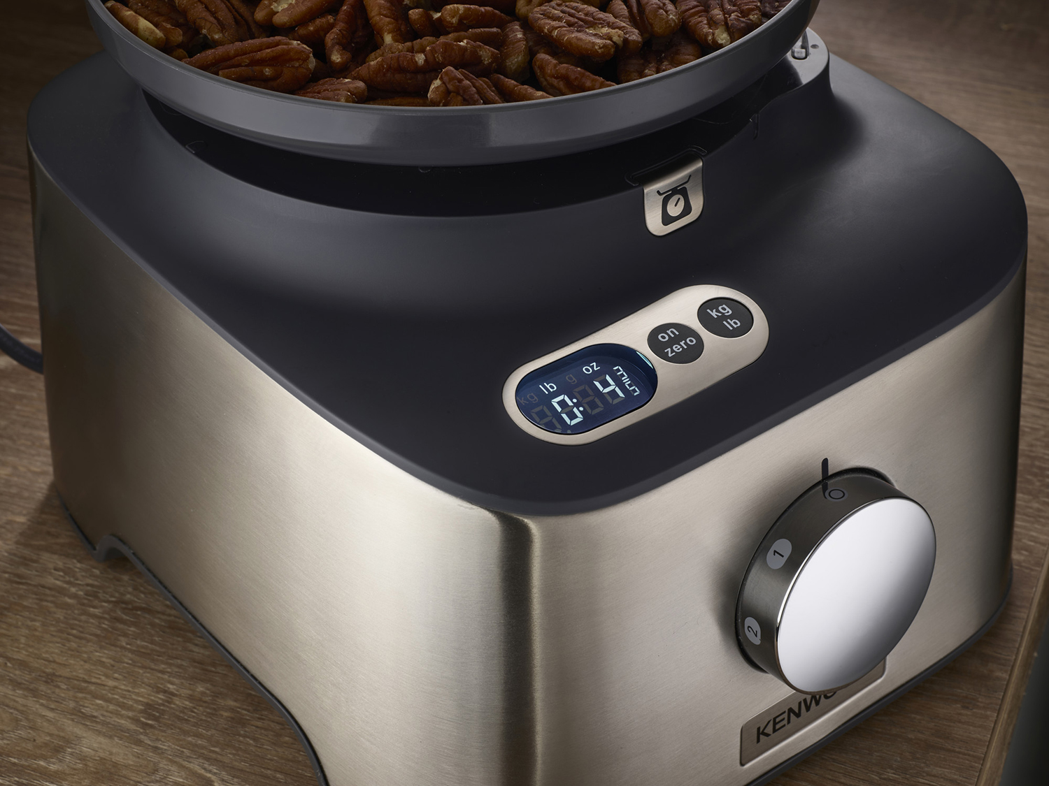 Close-up of a black and silver food processor with a digital display and a bowl of pecans.