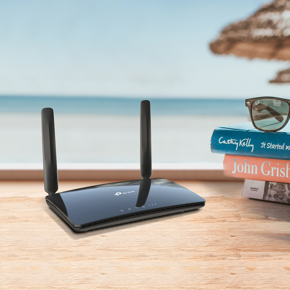 Un routeur noir avec deux antennes sur une table en bois avec des livres et une vue sur la mer.