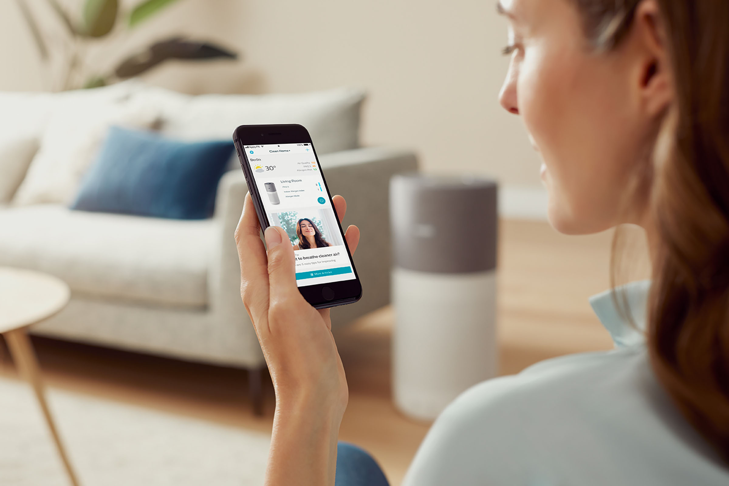 Eine Frau, die ein Telefon hält und eine Smart-Home-App zeigt.