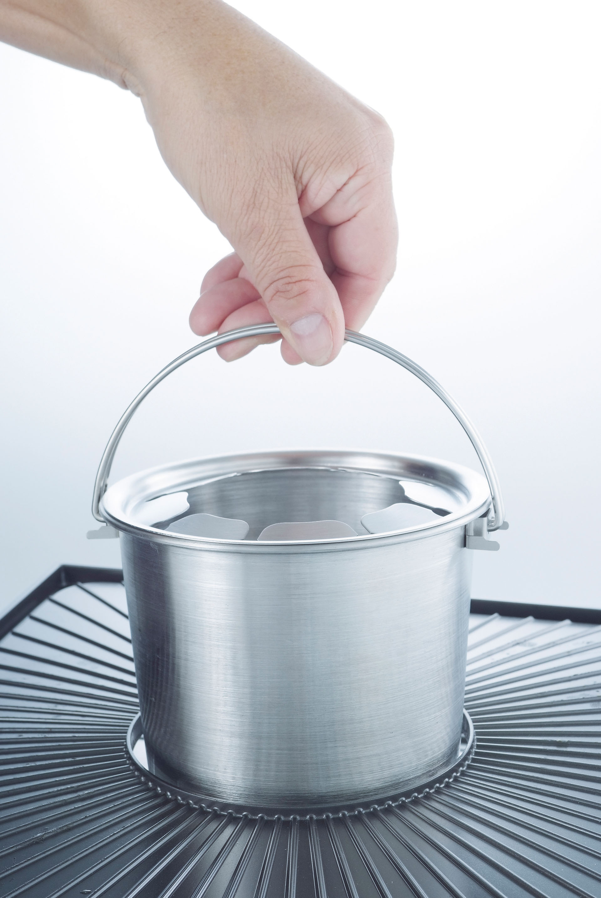 Hand hält silbernen Eimer mit Griff über schwarzem Metallständer.