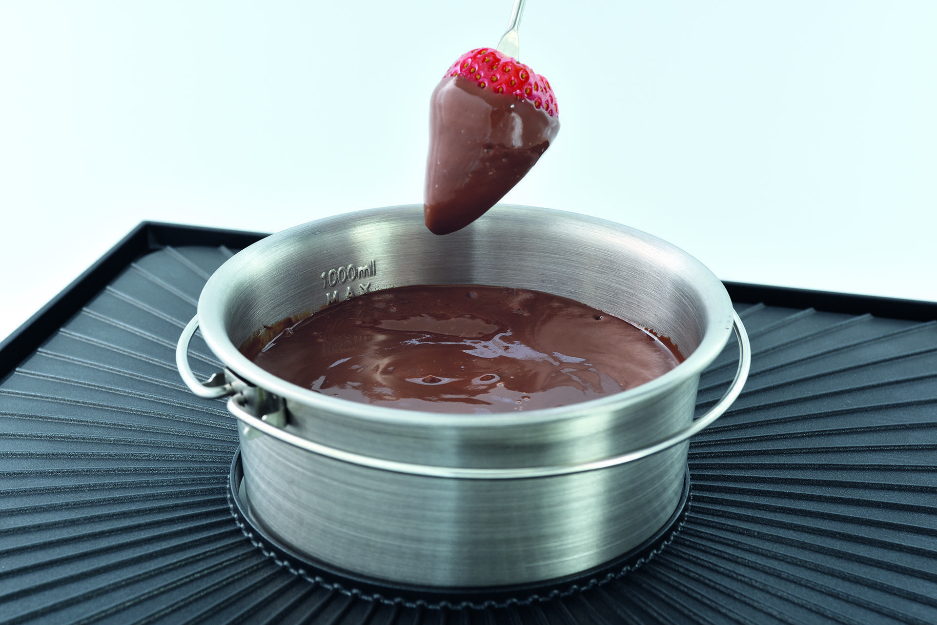 Eine in Schokolade getauchte Erdbeere wird über einer Schüssel mit geschmolzener Schokolade gehalten.