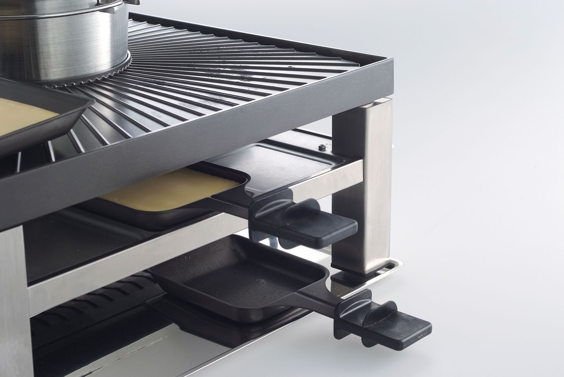 Ein Raclette-Grill, der die Grillplatte, die Käsetabletts und den Rahmen zeigt. Weißer Hintergrund.