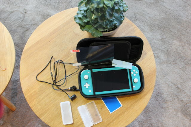 A teal Nintendo Switch Lite, case, and accessories on a wooden table.