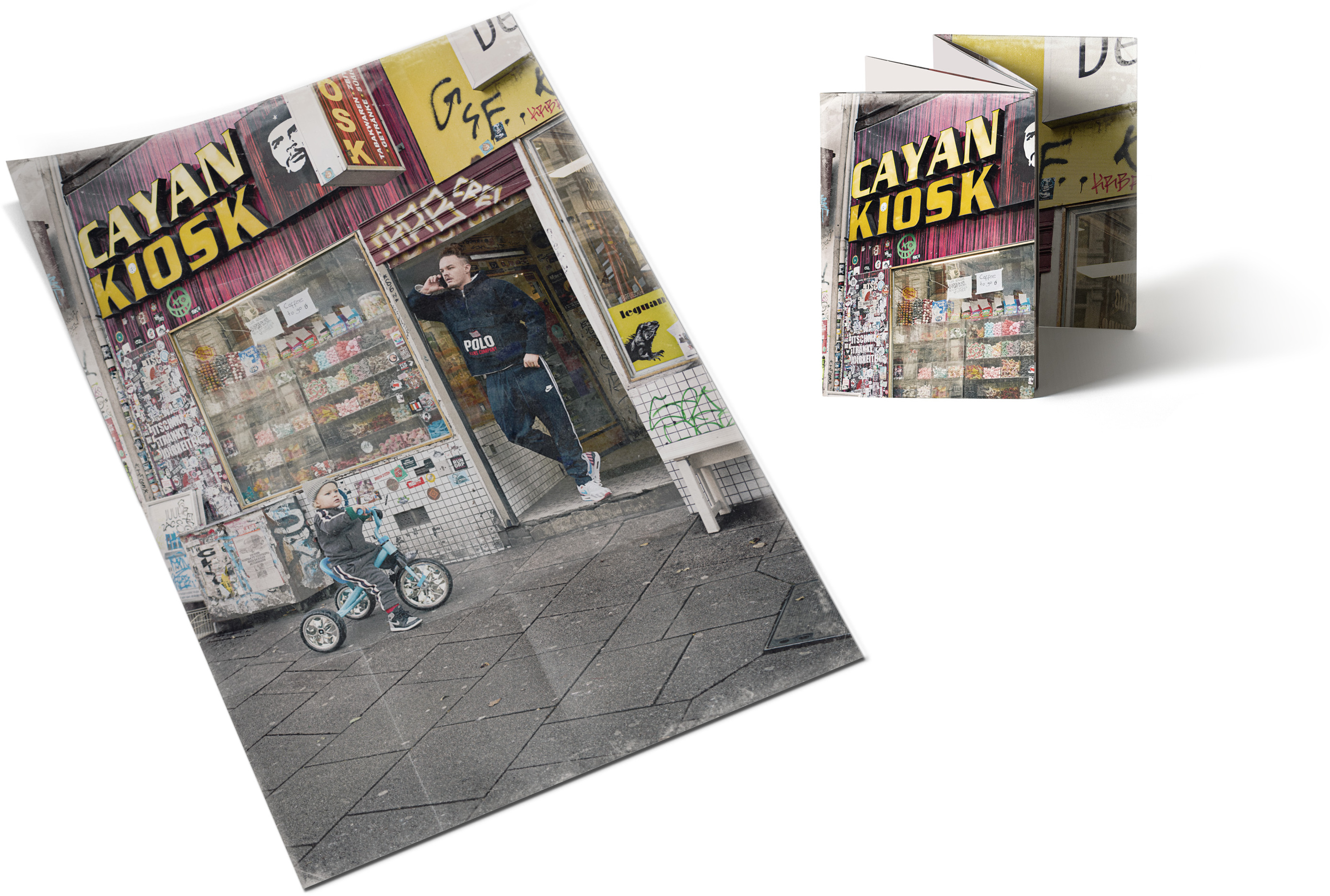 Ein gefaltetes Magazin mit einer Kiosk-Szene auf dem Cover, Menschen auf der Straße und einem Kind auf dem Fahrrad.