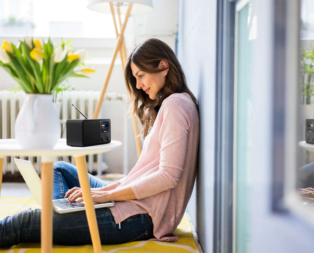 Een vrouw zit op de grond met een laptop en een radio naast haar.
