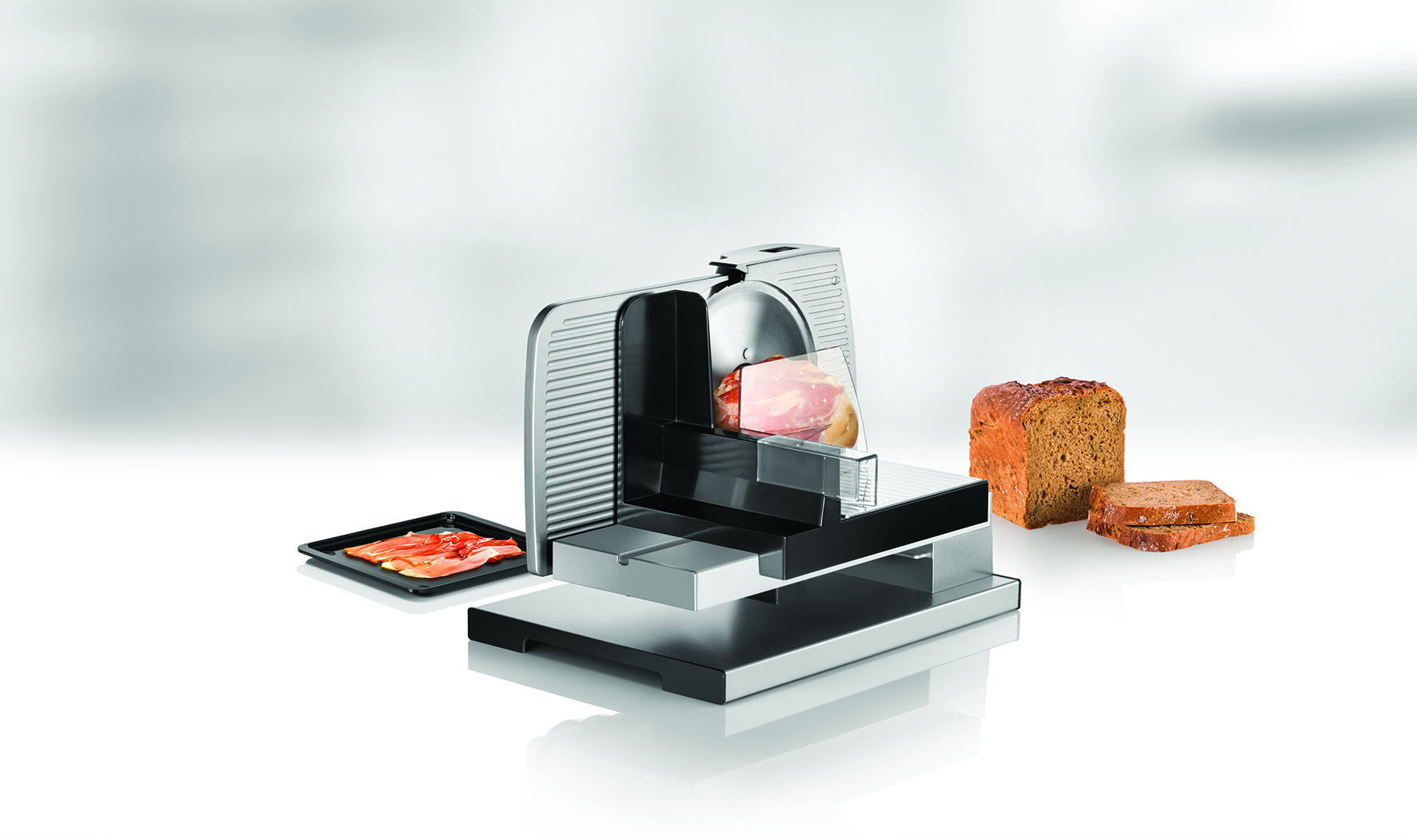 Fleischschneider mit Fleisch- und Brotscheiben. Eine Schale mit Fleisch links.