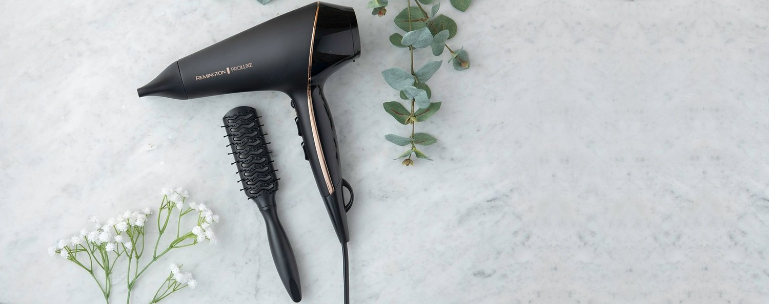 Sèche-cheveux, brosse et fleurs disposés sur une surface en marbre, vue de dessus.