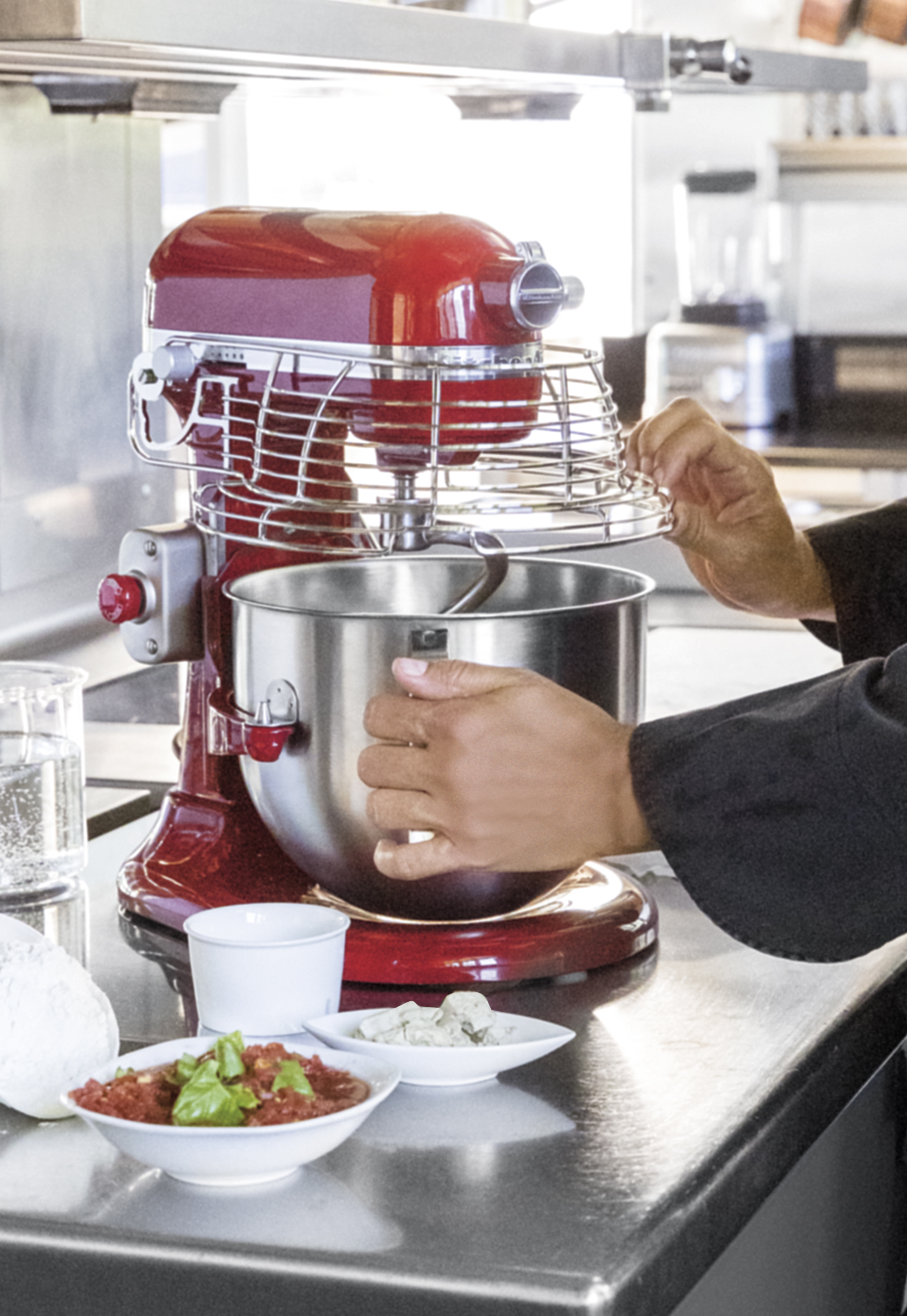 Ein roter Standmixer in einer Küche in Gebrauch. Zutaten auf der Theke: Schalen mit Essen, eine weiße Tasse und Mehl.