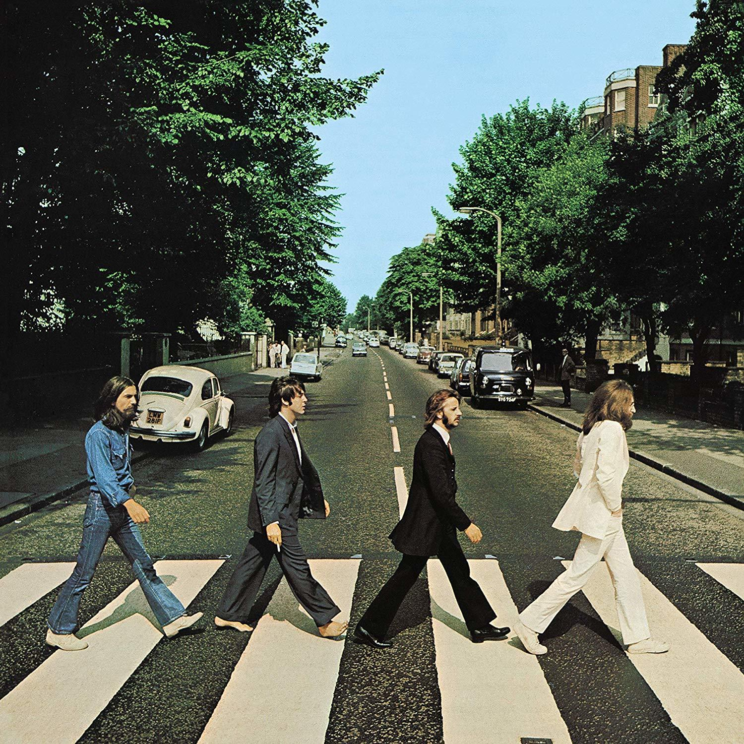 A Beatles átkelnek az Abbey Roadon, egy zebrán. Zöld fák szegélyezik az utcát. Autók vannak.