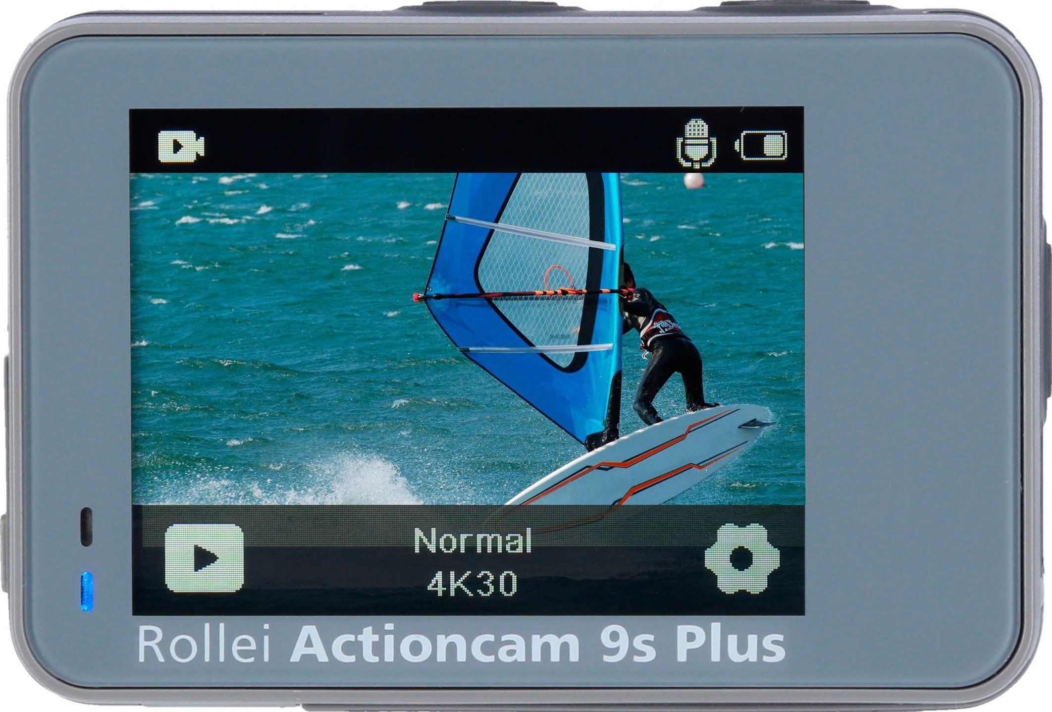 Schermo della action camera che mostra un windsurfista sull'acqua. Vela blu. Fotocamera grigia.