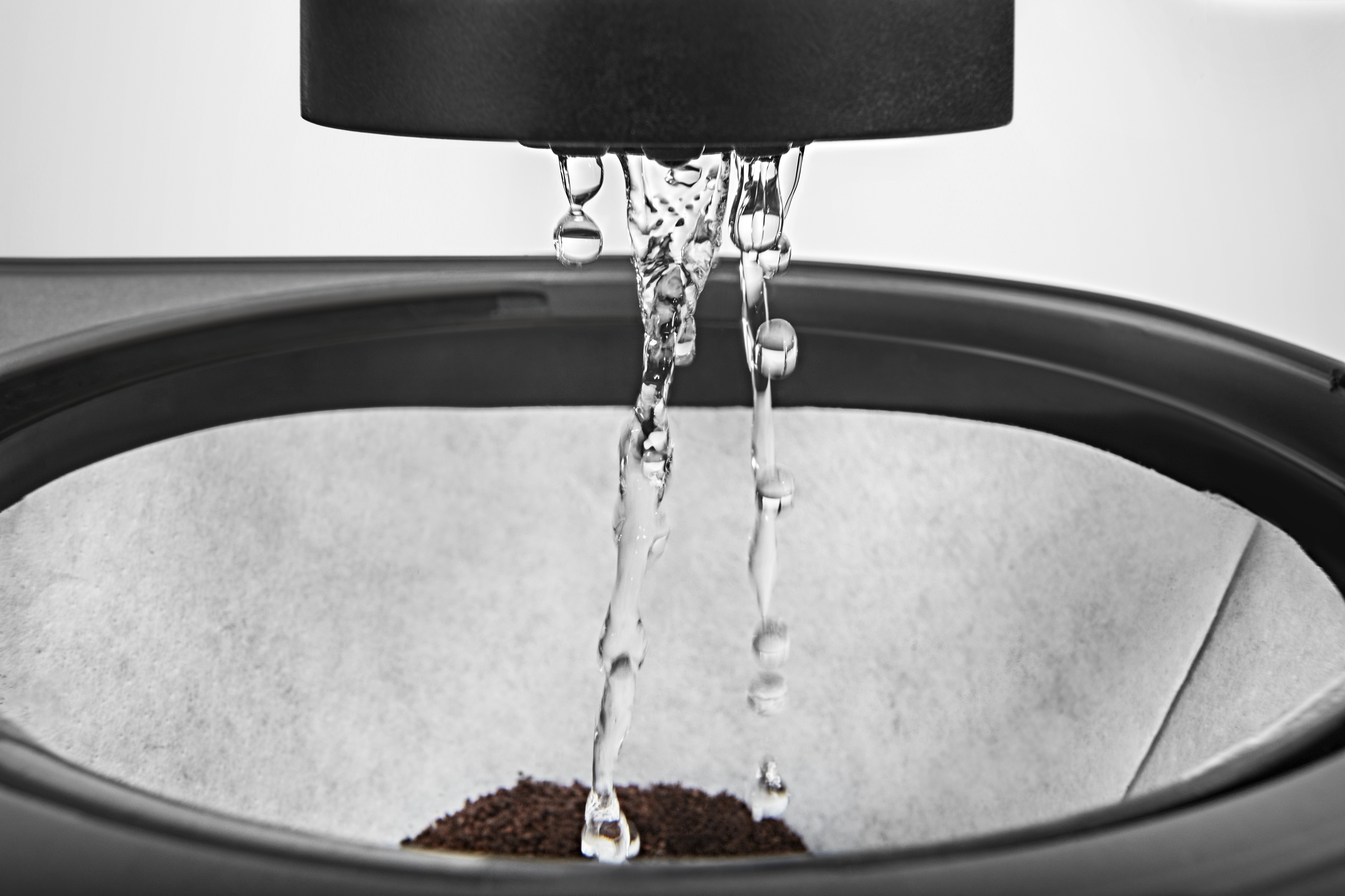 Nahaufnahme des Kaffeebrühens. Wasser tropft aus einer schwarzen Maschine auf Kaffeepulver in einem Filter und erzeugt einen klaren Strom.