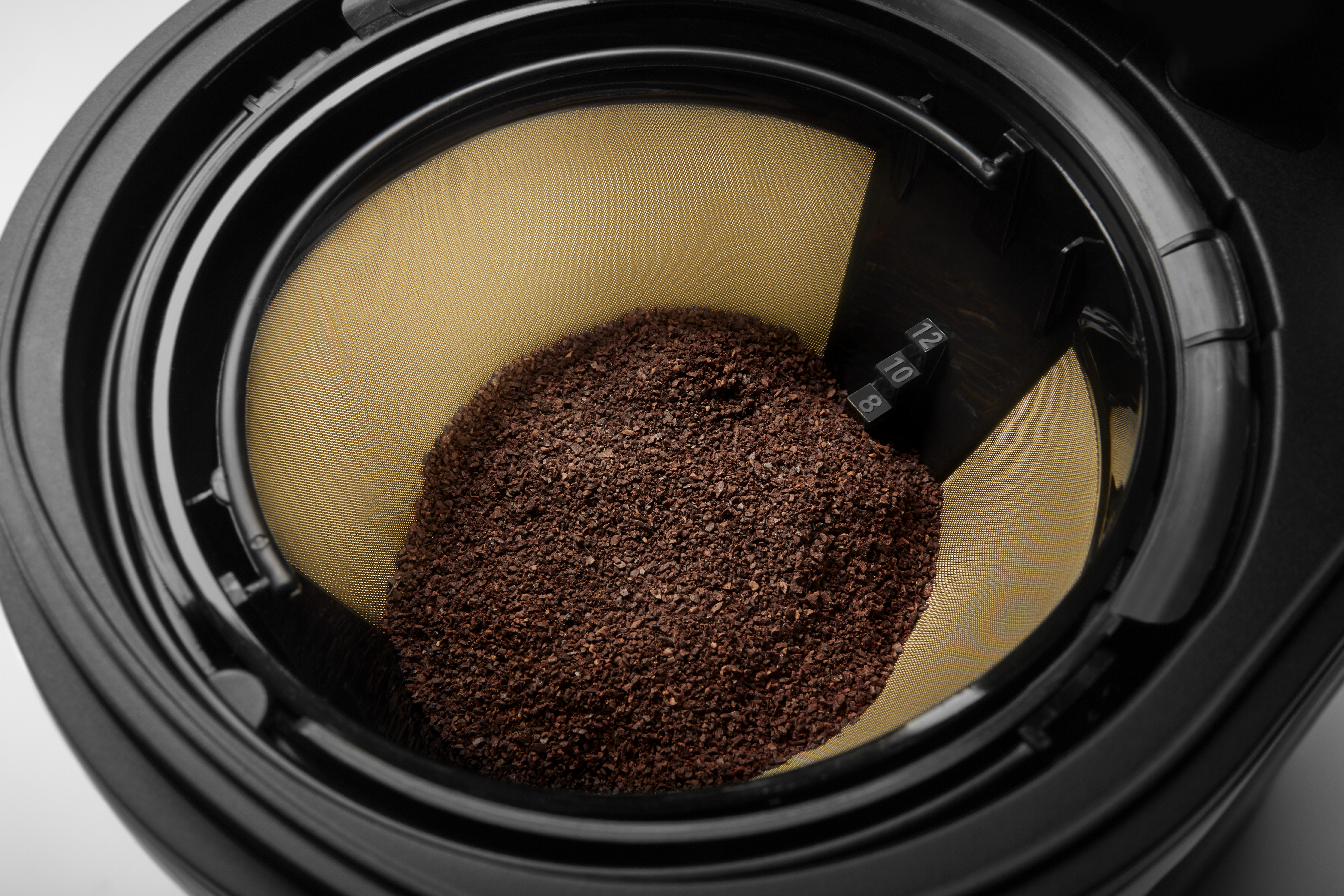 Nahaufnahme eines Kaffeefilters mit Kaffeepulver. Der Filter ist goldfarben, mit schwarzem Rahmen. Zahlen sind sichtbar.