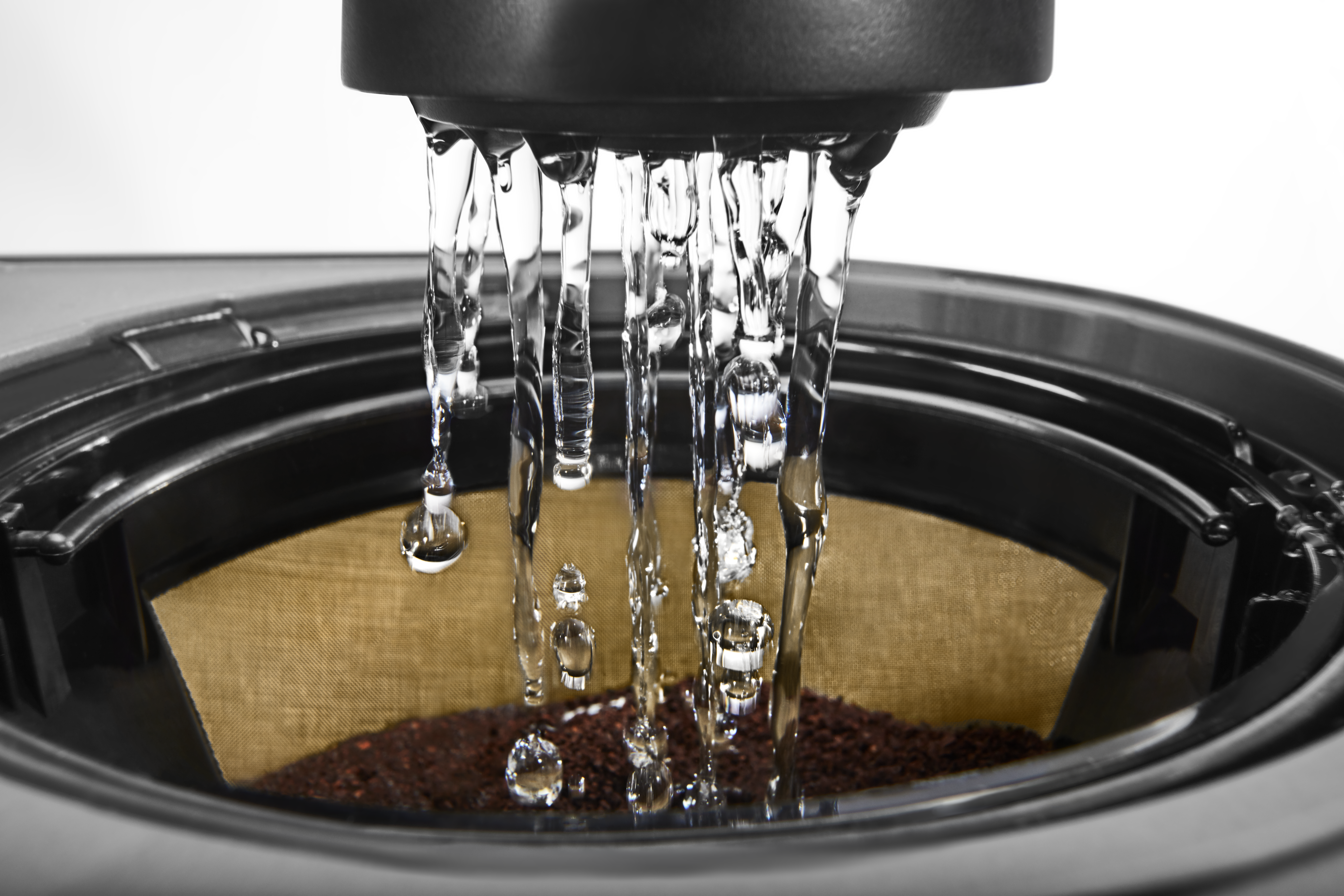 Wasser gießt in eine Kaffeemaschine. Wasserstrahlen fallen auf Kaffeepulver in einem Filter. Der Hintergrund ist weiß.