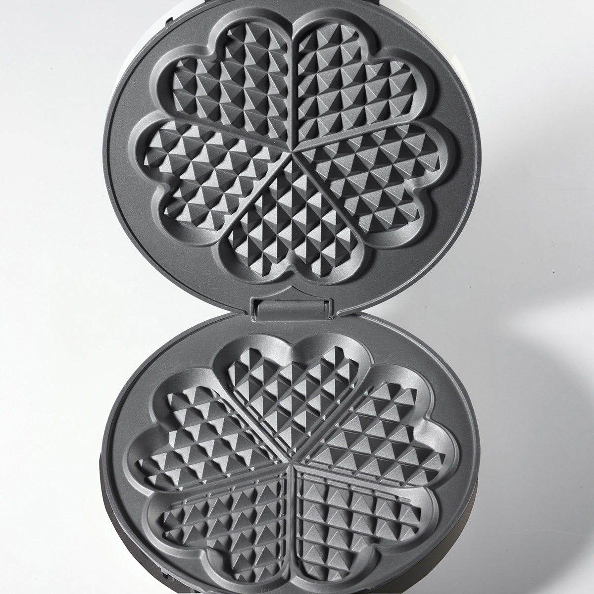 Waffeleisen, geöffnet, zeigt die Kochflächen mit herzförmigen Mustern.
