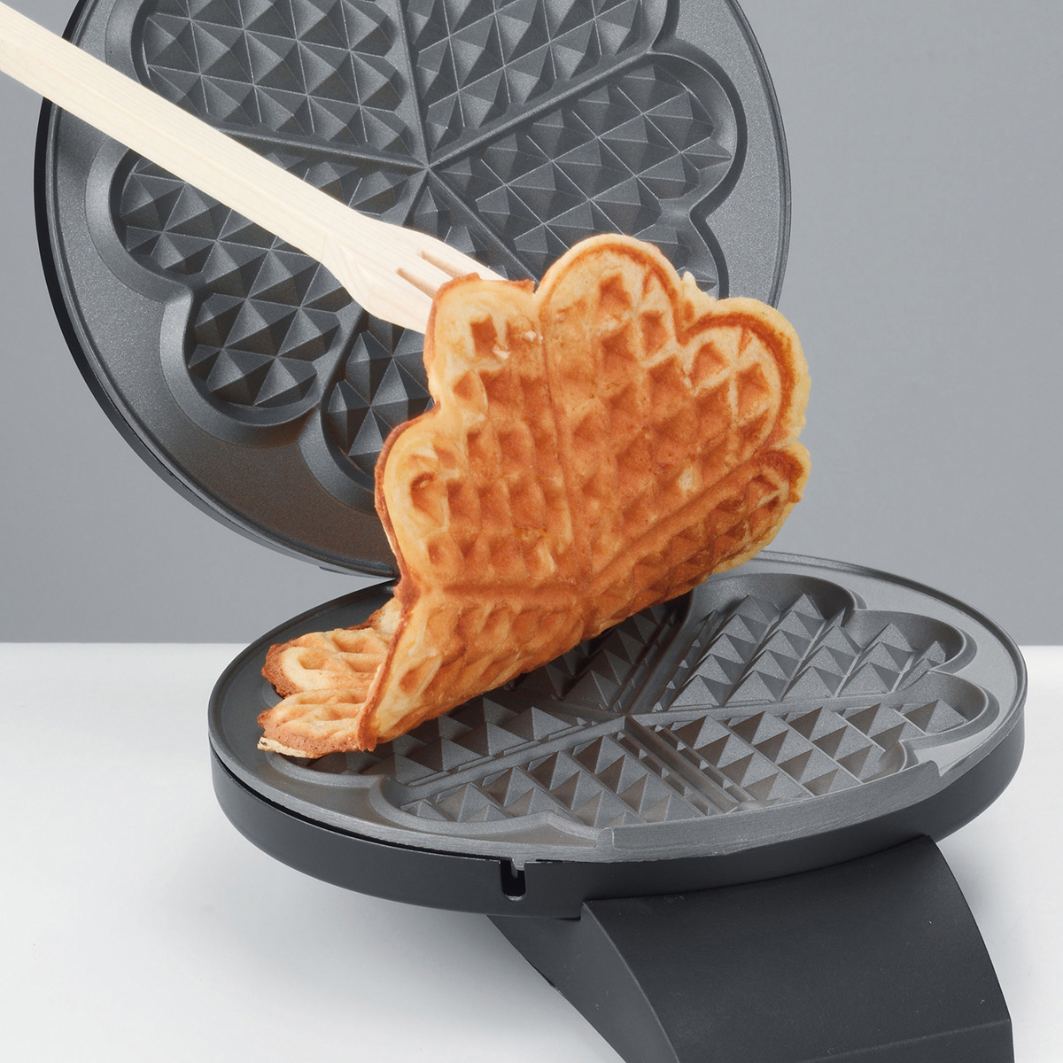 Waffeleisen mit Waffel. Die Waffel ist goldbraun und wird mit einer Gabel entnommen.