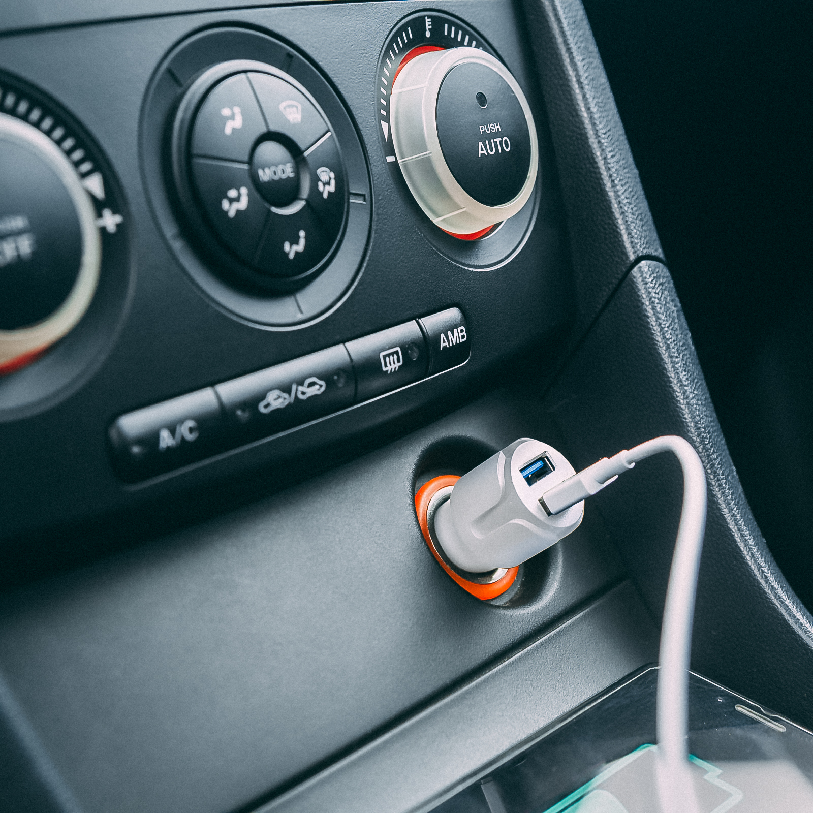 Egy autó műszerfalának közeli képe. Egy fehér és szürke USB-töltő van az autó aljzatába dugva.