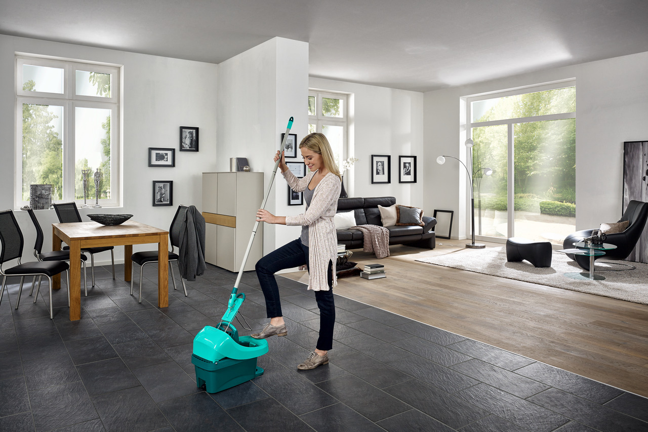 Eine Frau wischt einen schwarzen Fliesenboden in einem modernen Wohnzimmer mit Möbeln.