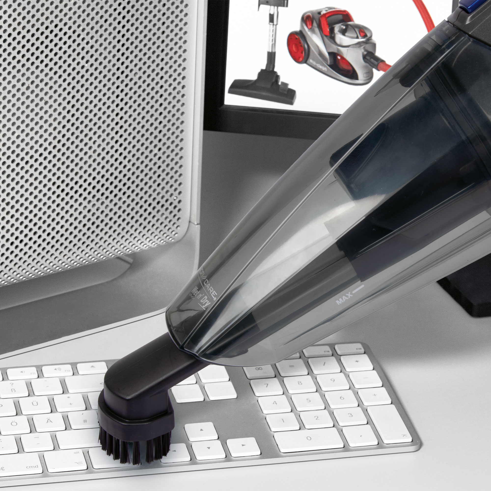 Staubsauger reinigt eine Tastatur. Computermonitor und Staubsauger sind sichtbar.