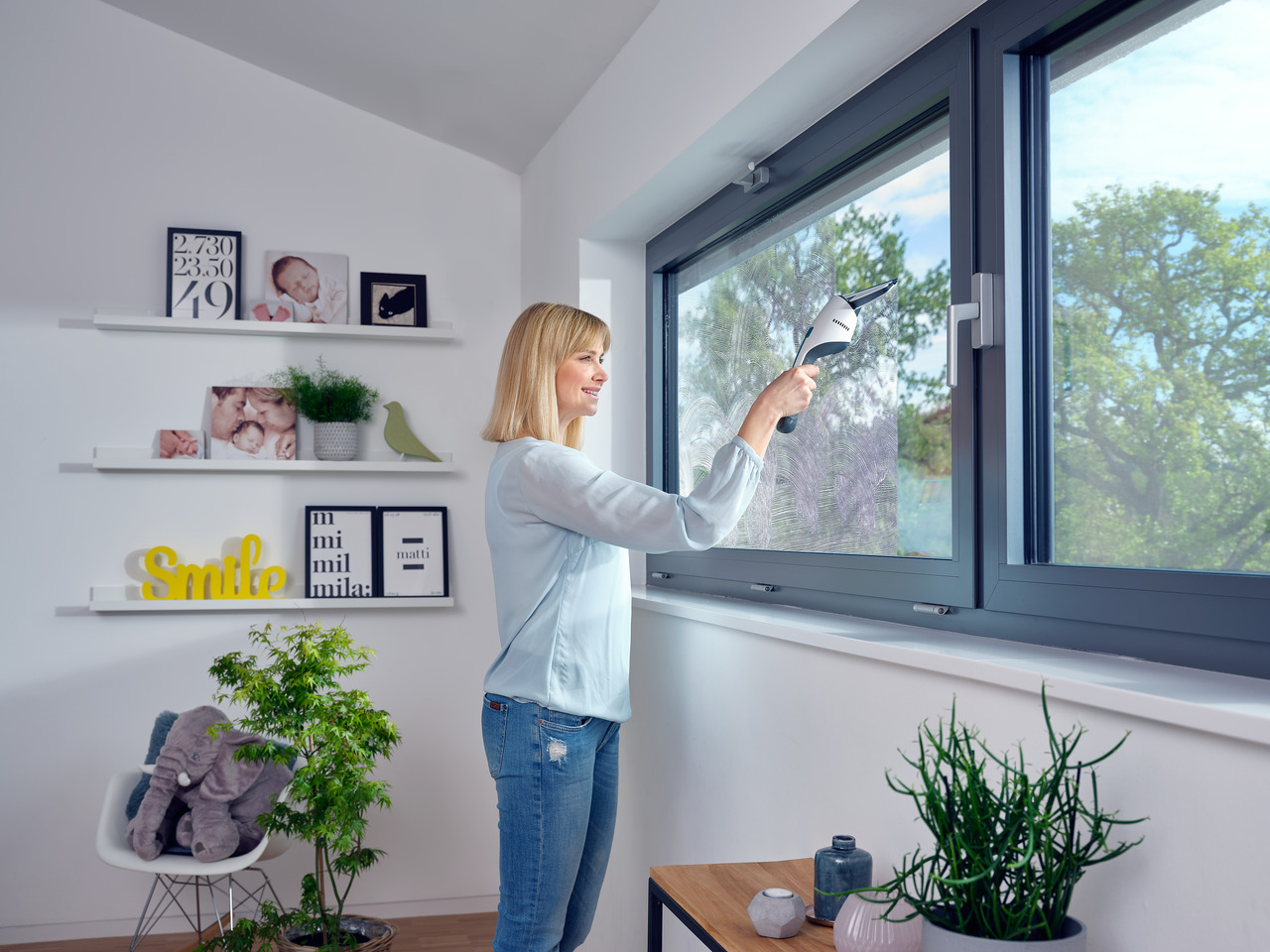 Eine Frau reinigt ein Fenster mit einem Reiniger, mit Pflanzen und Dekoration im Raum.