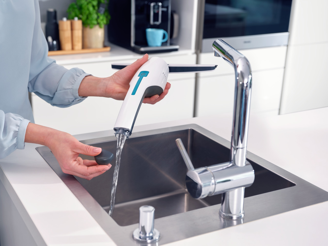 Frau benutzt ein weißes und blaues Wasserreinigungswerkzeug an einem Waschbecken. Silberner Wasserhahn.