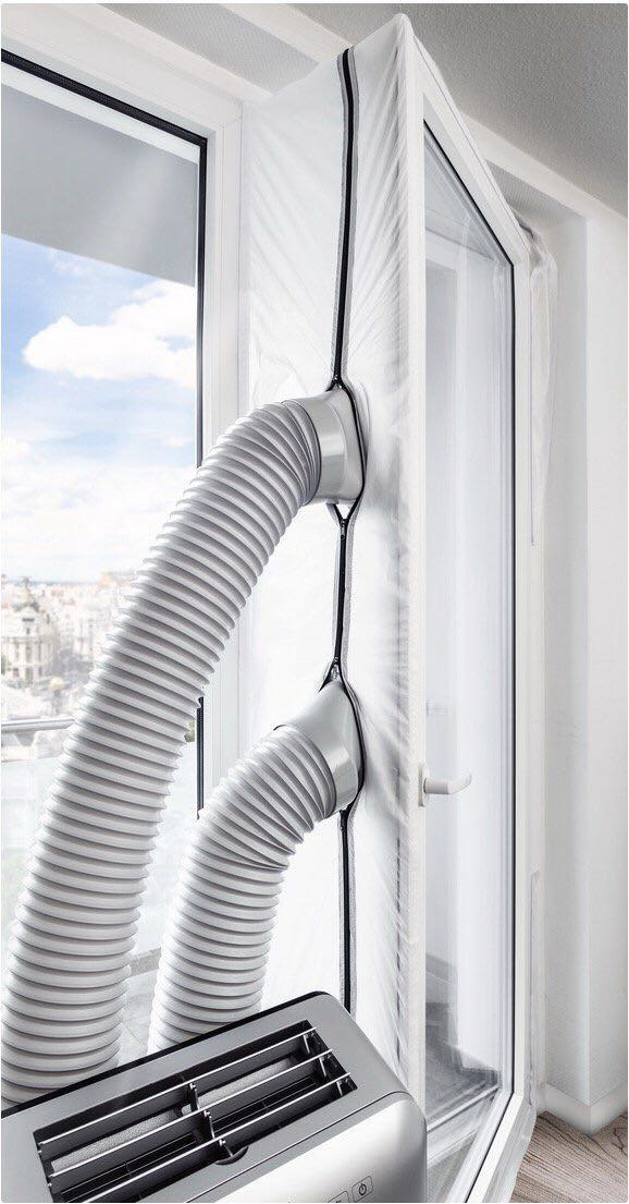 Klimaanlage in einem Fenster installiert. Zwei graue Rohre führen nach draußen. Stadtbild durch Fenster sichtbar.