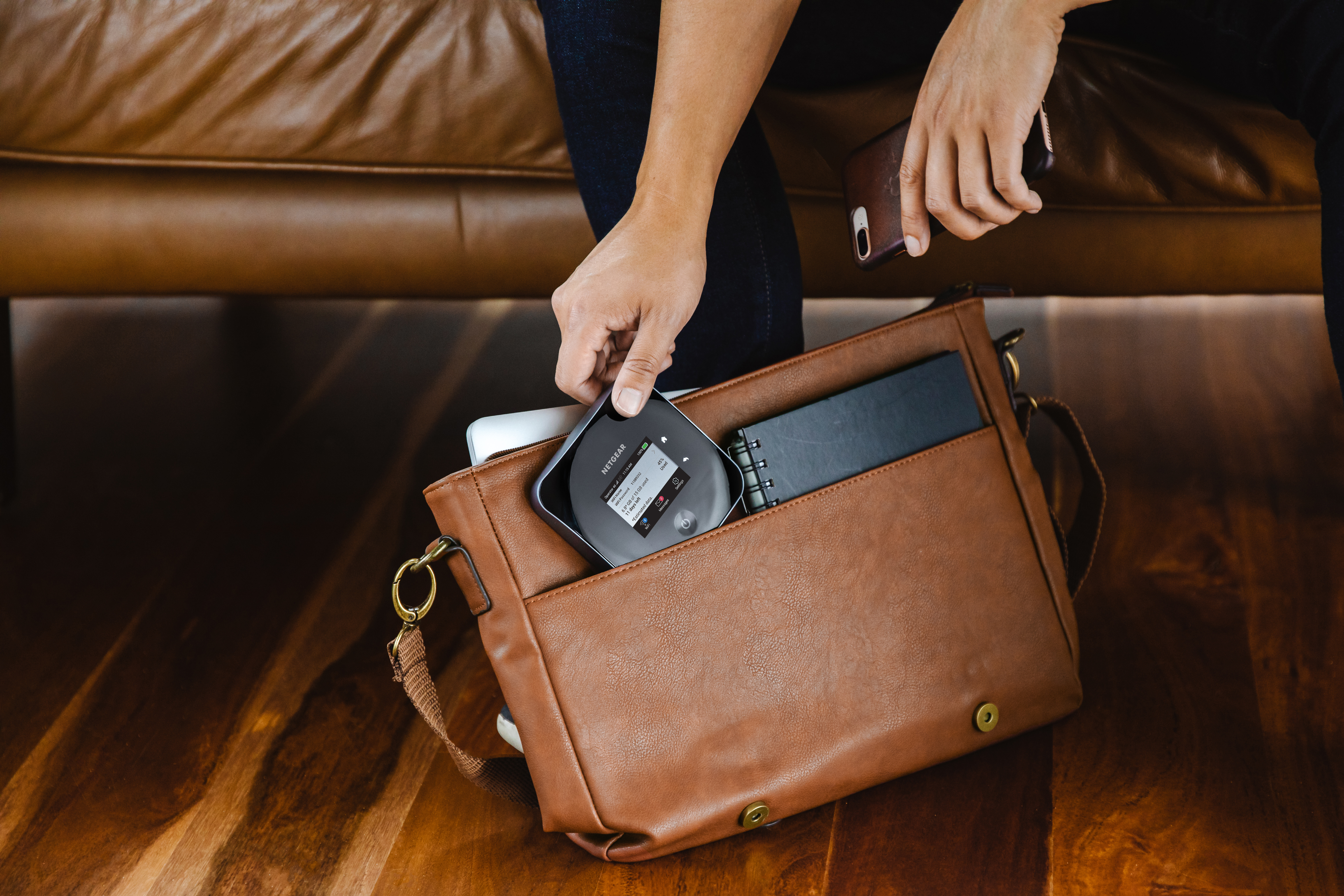 A person putting a mobile hotspot into a brown bag, sitting on a brown leather couch.