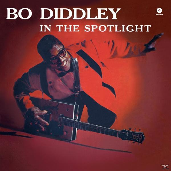 Bo Diddley, szemüveggel és piros kabáttal, gitárt tart. Album borító, piros háttér, 'In the Spotlight' felirat.