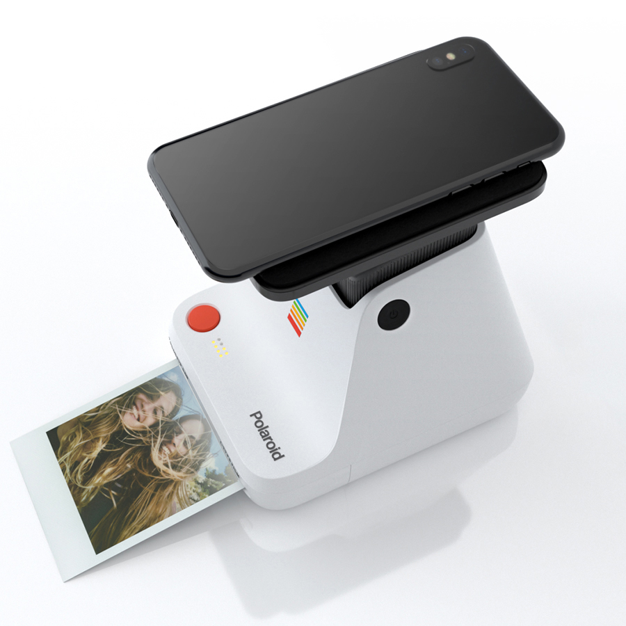 Weiße Polaroid-Kamera, die ein Foto druckt, mit einem schwarzen Telefon oben und einem gedruckten Foto.
