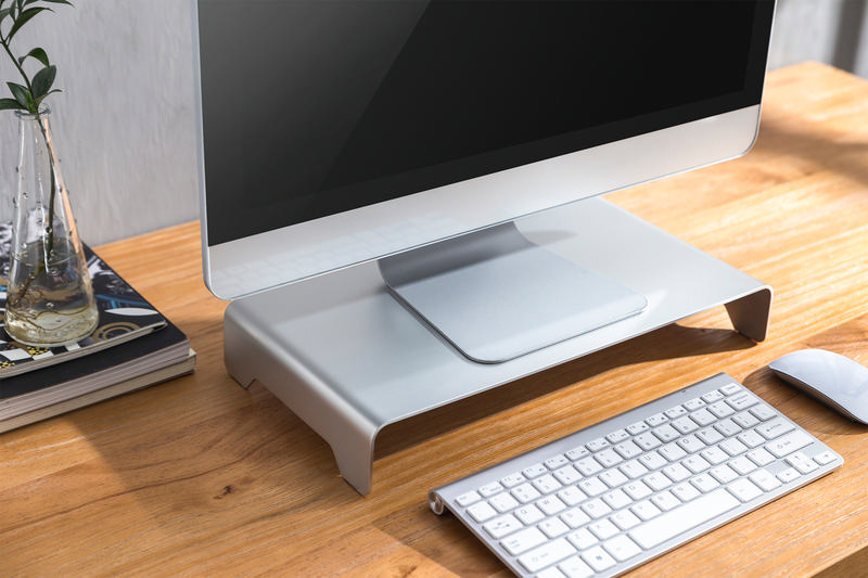 Silberner Monitorständer mit Computer, Tastatur und Maus auf einem Holztisch.