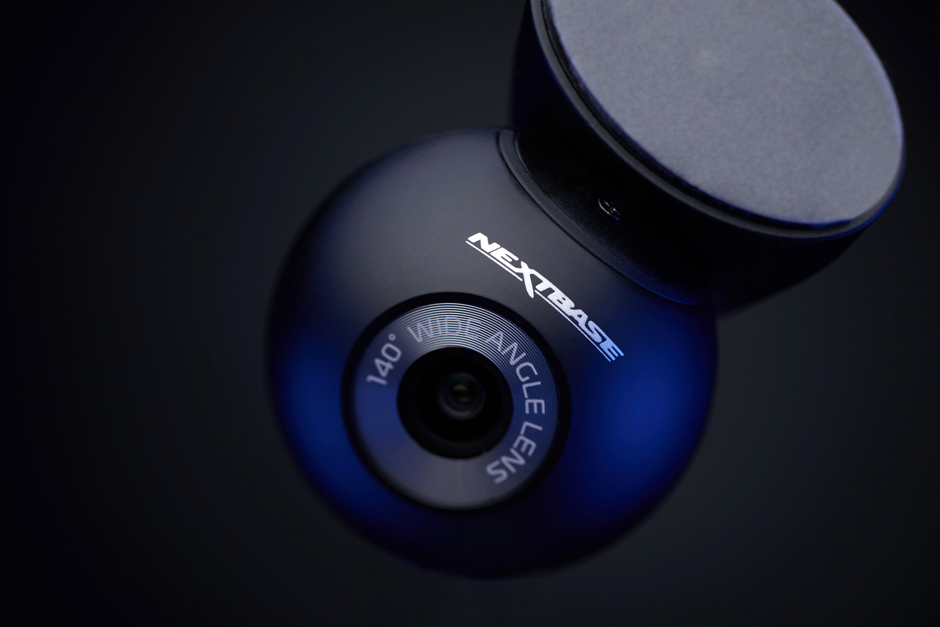Caméra de tableau de bord noire et ronde avec le logo "NEXTBASE" et un objectif grand angle. Le support est en haut.
