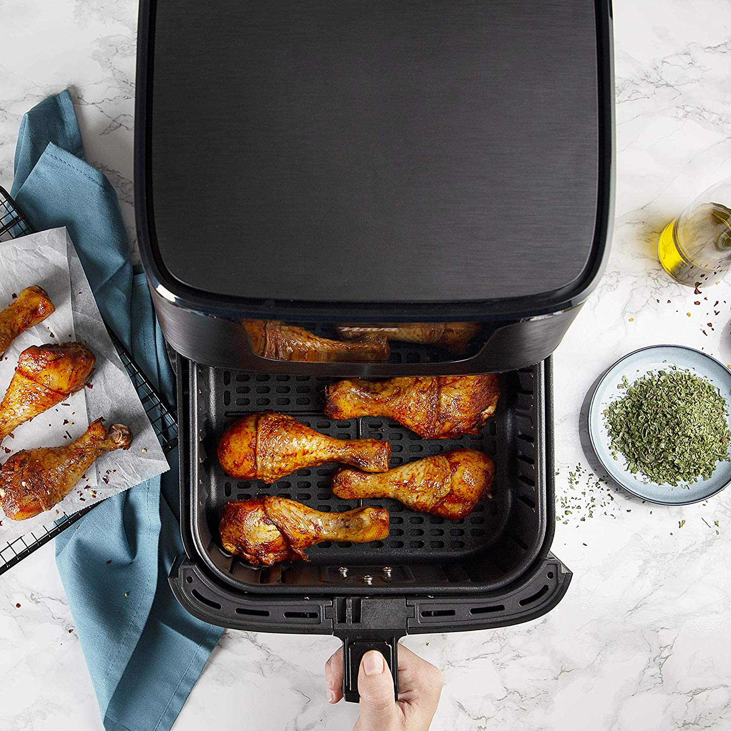 Air fryer with cooked chicken drumsticks.  Oil bottle and spice jar are on the side.