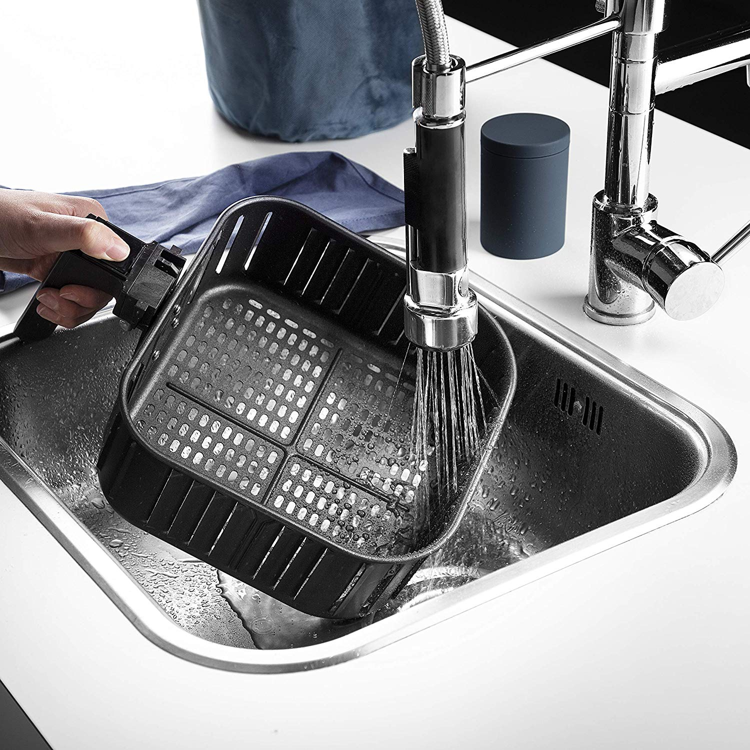A black air fryer basket is being washed in a stainless steel sink.