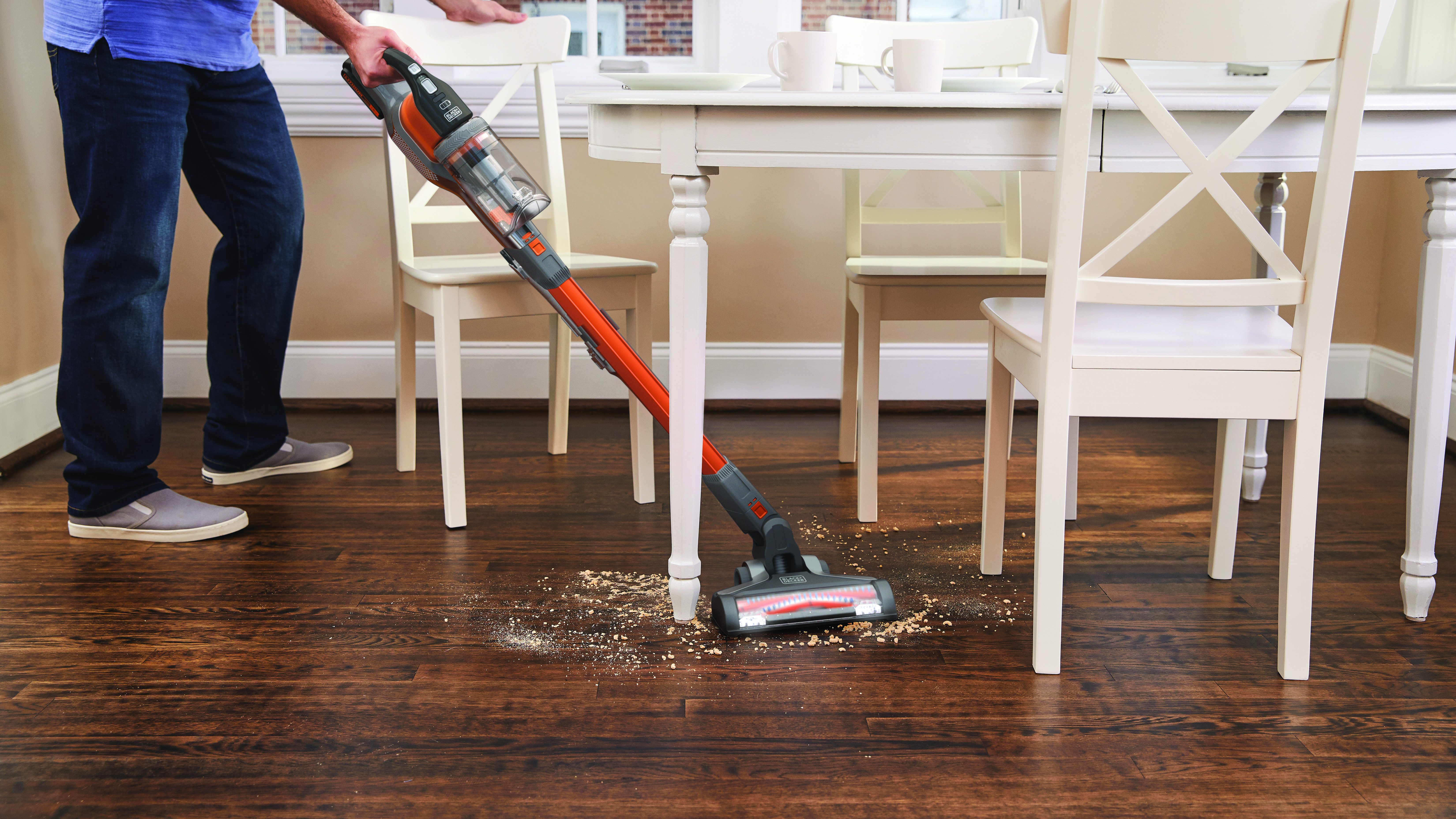 A person vacuuming a wooden floor. A table and chairs are nearby.
