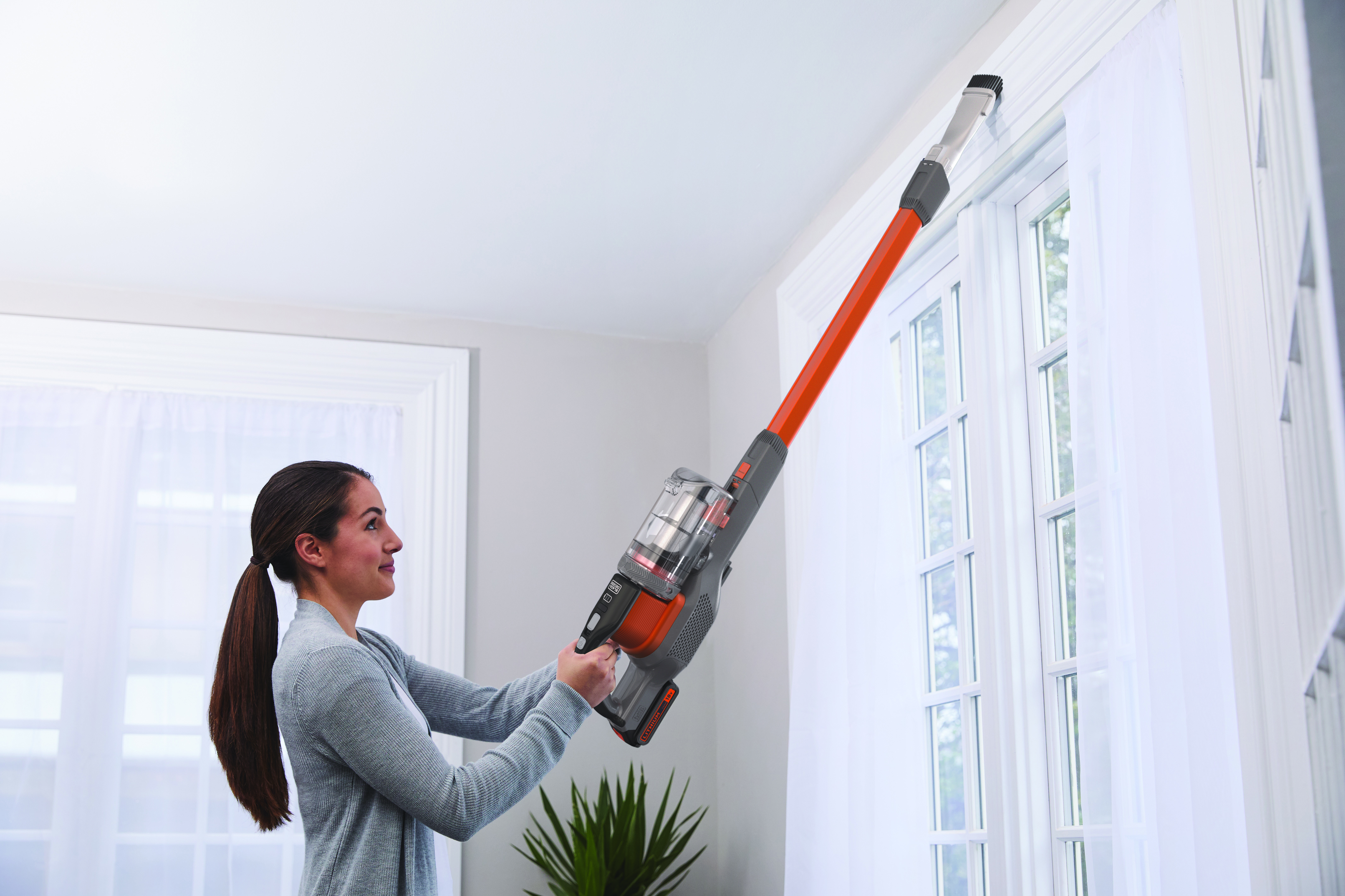 Woman vacuuming near a window with a cordless vacuum cleaner.