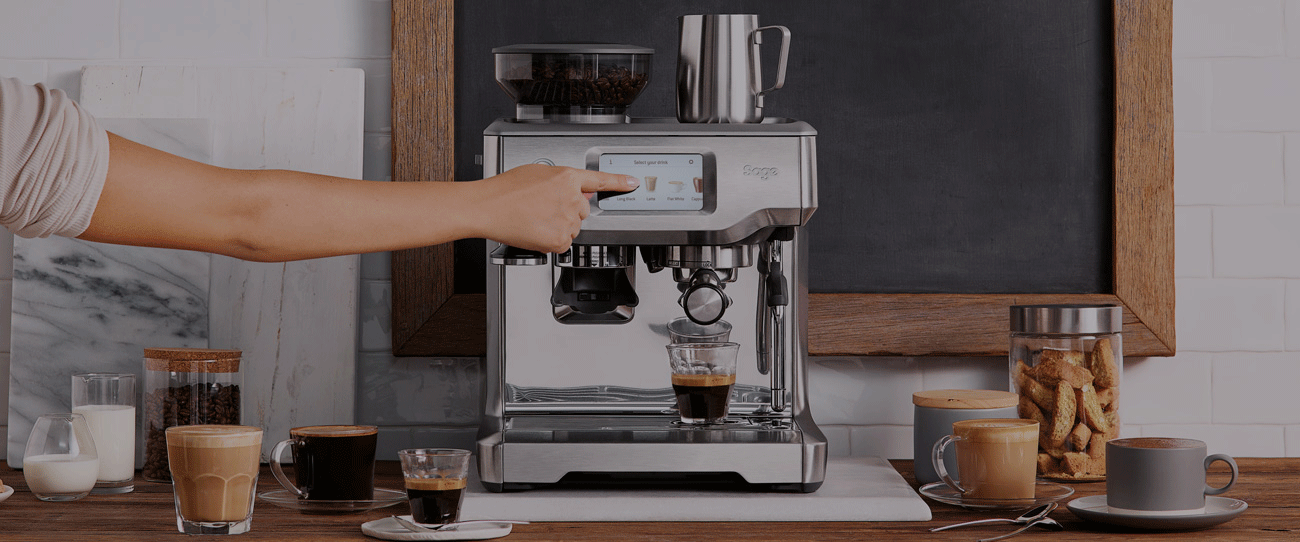 Une main touche l'écran d'une machine à café. Plusieurs boissons au café sont sur le comptoir. Il y a des biscuits dans un bocal.