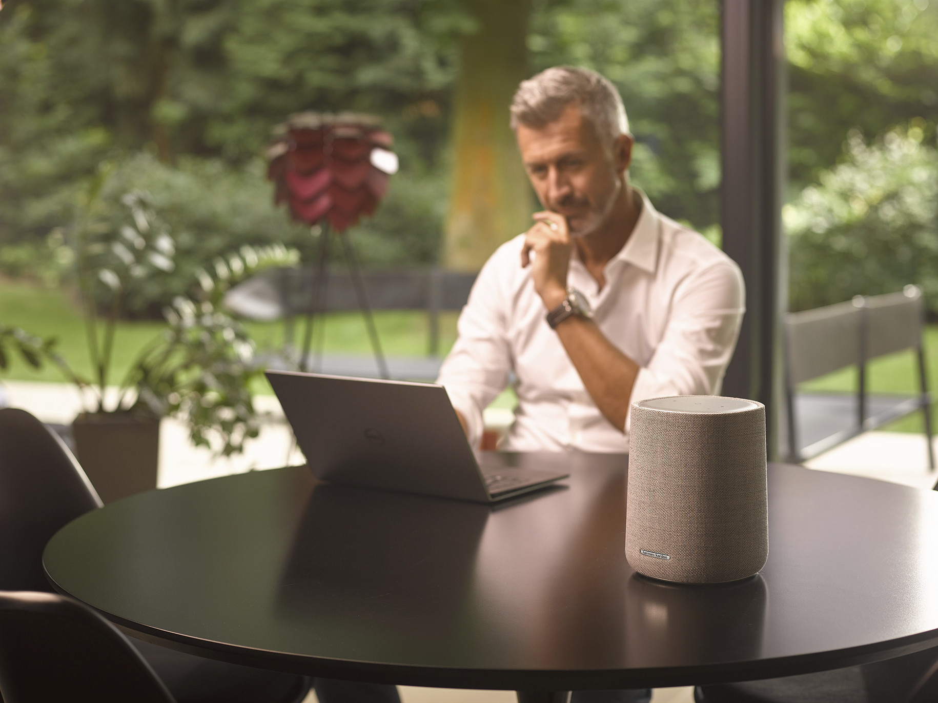 Een man zit aan een tafel met een laptop, met een luidspreker voor zich en een wazige achtergrond.
