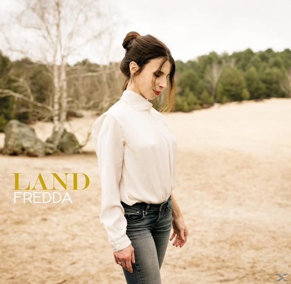 Albumcover 'Land' von Fredda, eine Frau in weißem Oberteil und Jeans, die in einer Wüstenlandschaft steht.