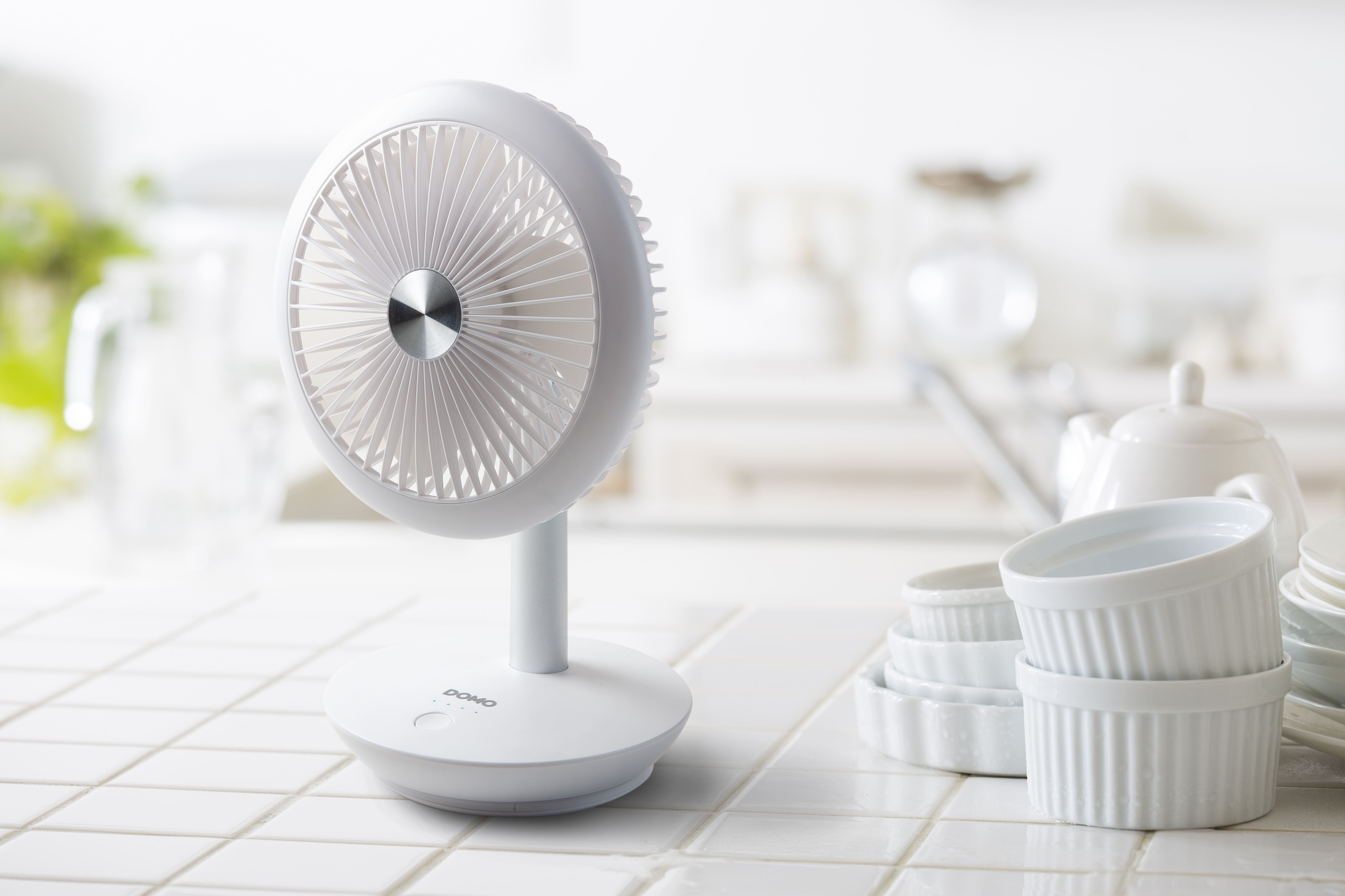 White fan on a white tiled surface with kitchen utensils in the background.