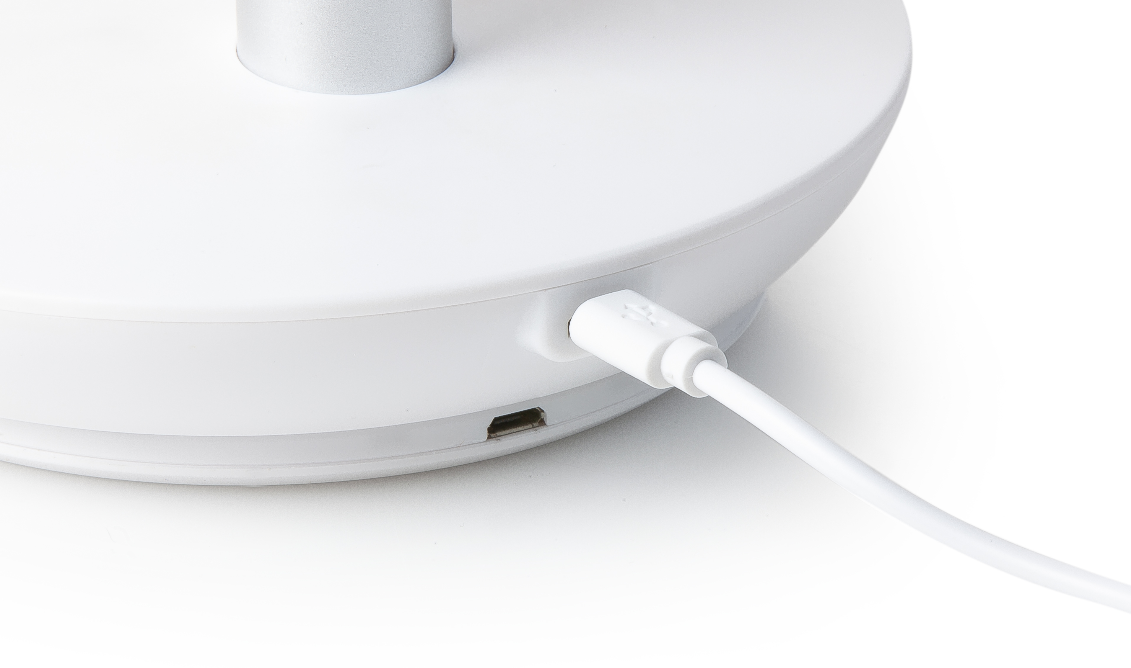 A white device with a USB-C port and a white USB cable plugged in. The device is on a white surface.