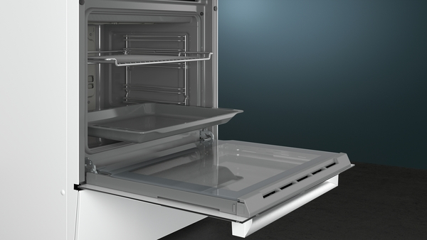 An open white oven with trays inside, set against a dark blue wall.