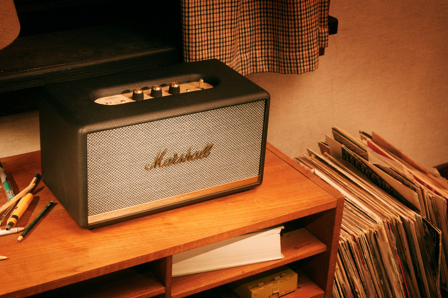 Gros plan d'un haut-parleur sur une étagère en bois avec des disques vinyles et des crayons à proximité.