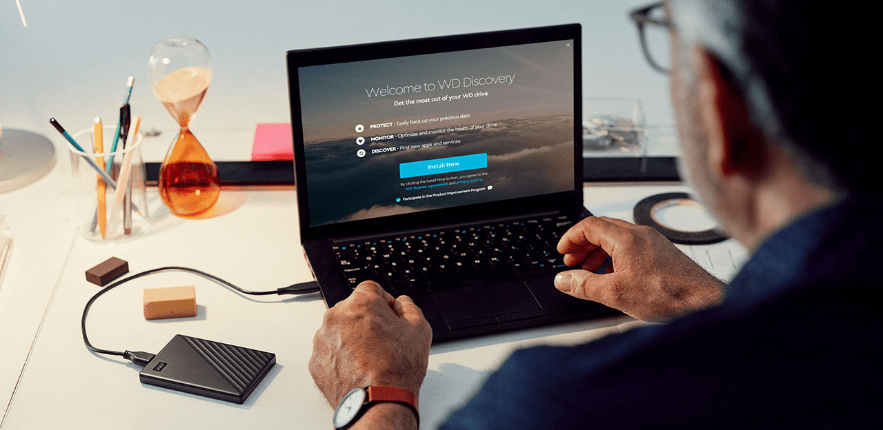 Un homme utilisant un ordinateur portable connecté à un disque dur portable sur un bureau blanc.