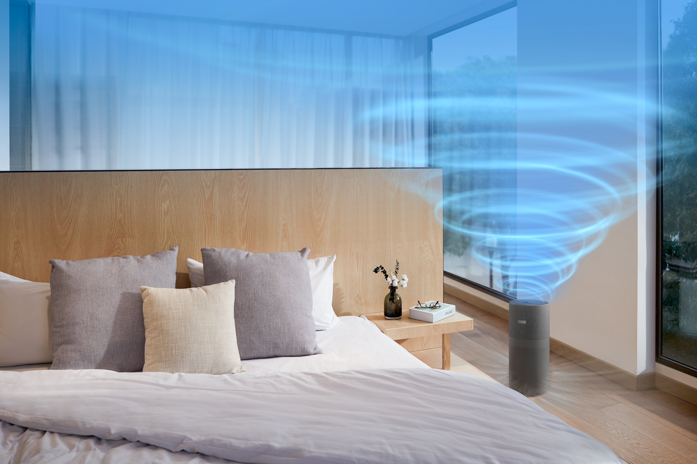 Een slaapkamer met een bed, kussens en een luchtreiniger met blauwe luchtstroom.